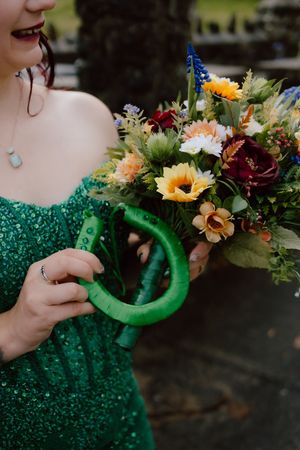 A green glittery horseshoe decorated with vibrant sunflowers and wildflowers being held against a dark background.