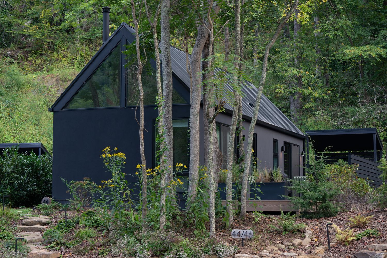 Exterior photograph of a modern vacation rental cabin in Western North Carolina surrounded by woodland and blooming flowers