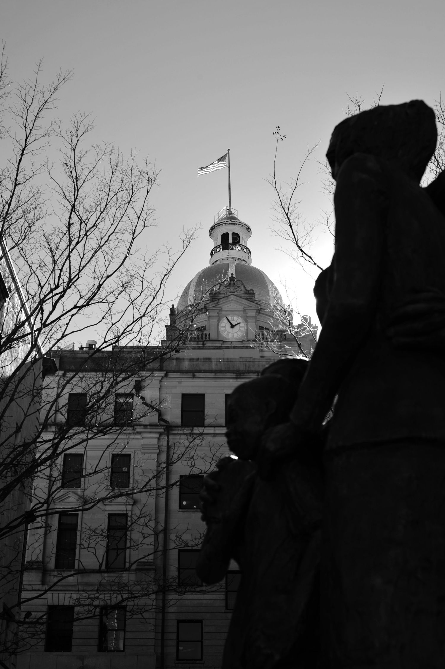 A black and white photo series showing the silhouette of a domed building against a moody sky with bare tree branches.