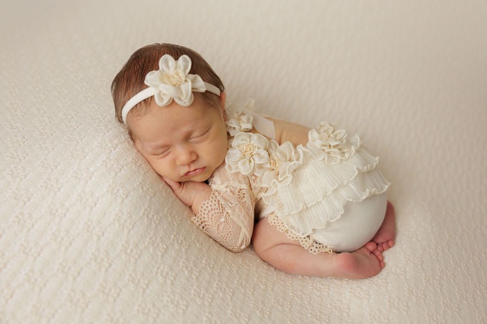 Sleeping newborn in cream wrap and floral headband posed on light background.