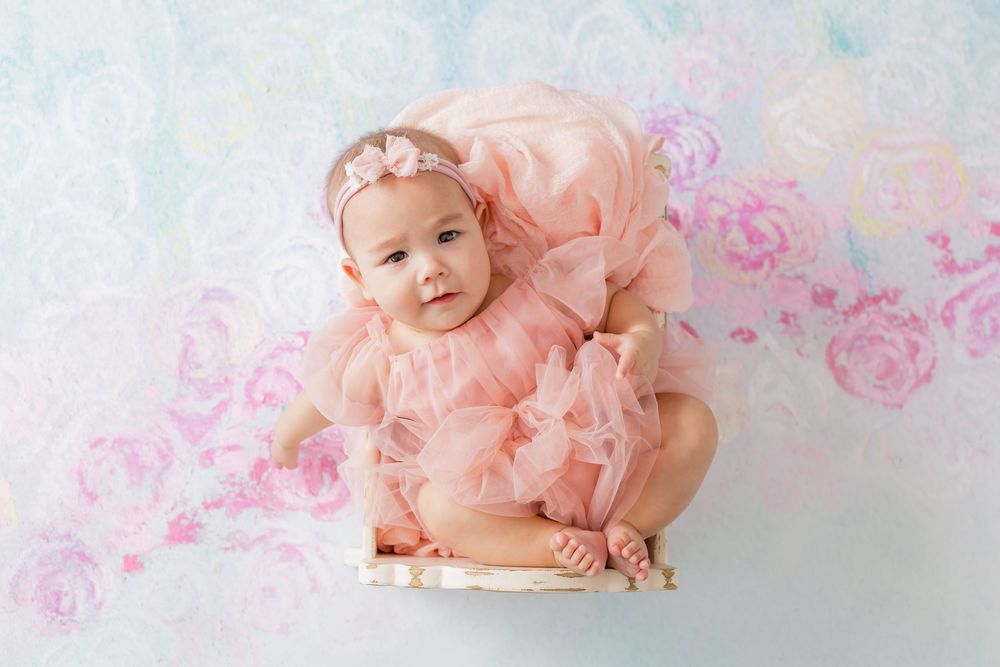 Sweet newborn photography session with pink floral decorations and soft pastel tones.