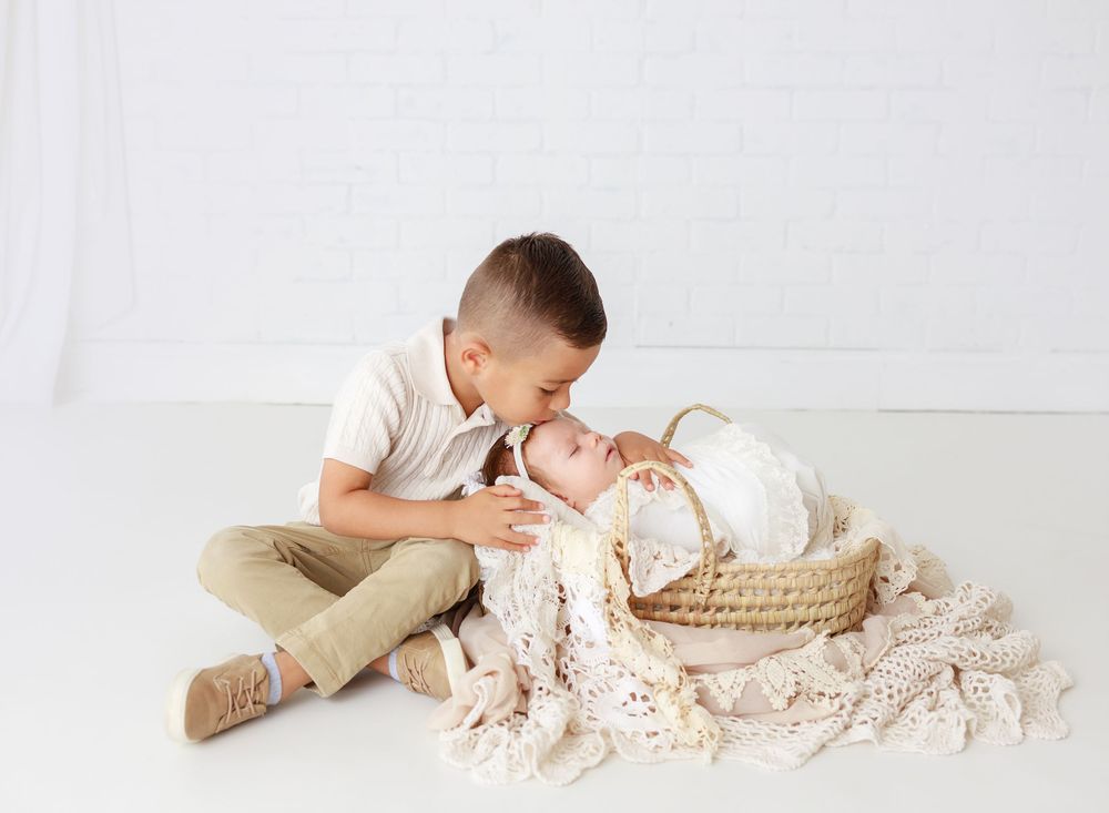 Tender sibling moment captured during newborn photo session on white backdrop.
