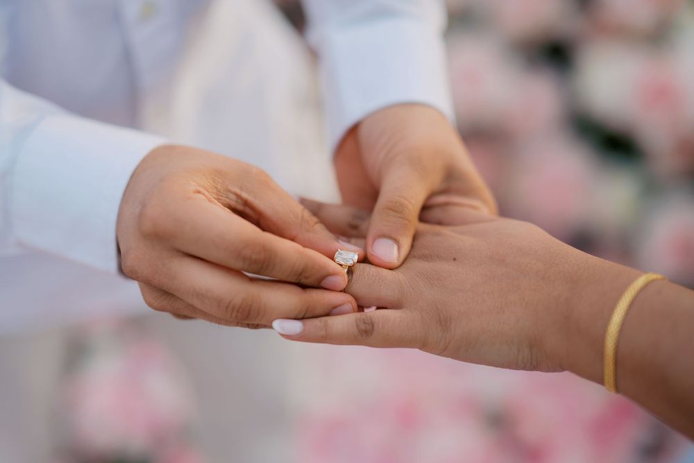 Close-up of hands exchanging wedding rings during a traditional ceremony with soft pink floral background.