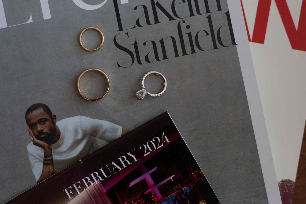 Gold rings and a diamond engagement ring rest on magazines featuring LaKeith Stanfield and a February 2024 issue.