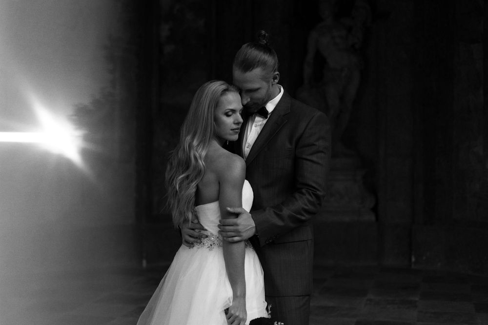 Black and white wedding photo of bride in strapless gown and groom in suit sharing intimate moment.