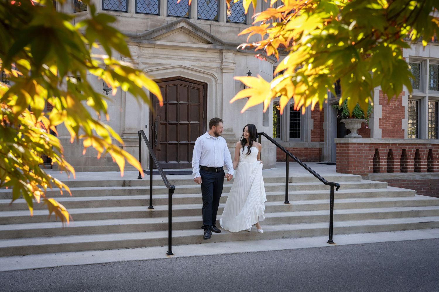 an elegant couple pose next to a building surrounded by golden autumn foliage at sunset.