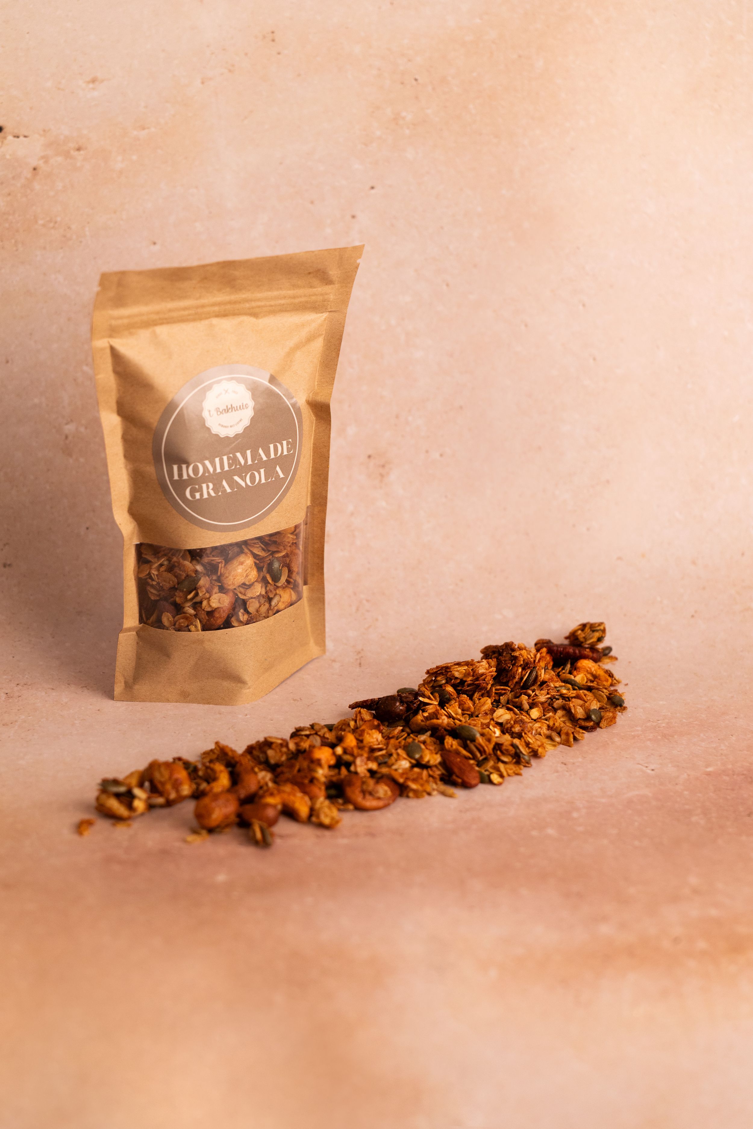 Kraft paper bag of homemade granola with scattered crunchy clusters on a warm beige background.