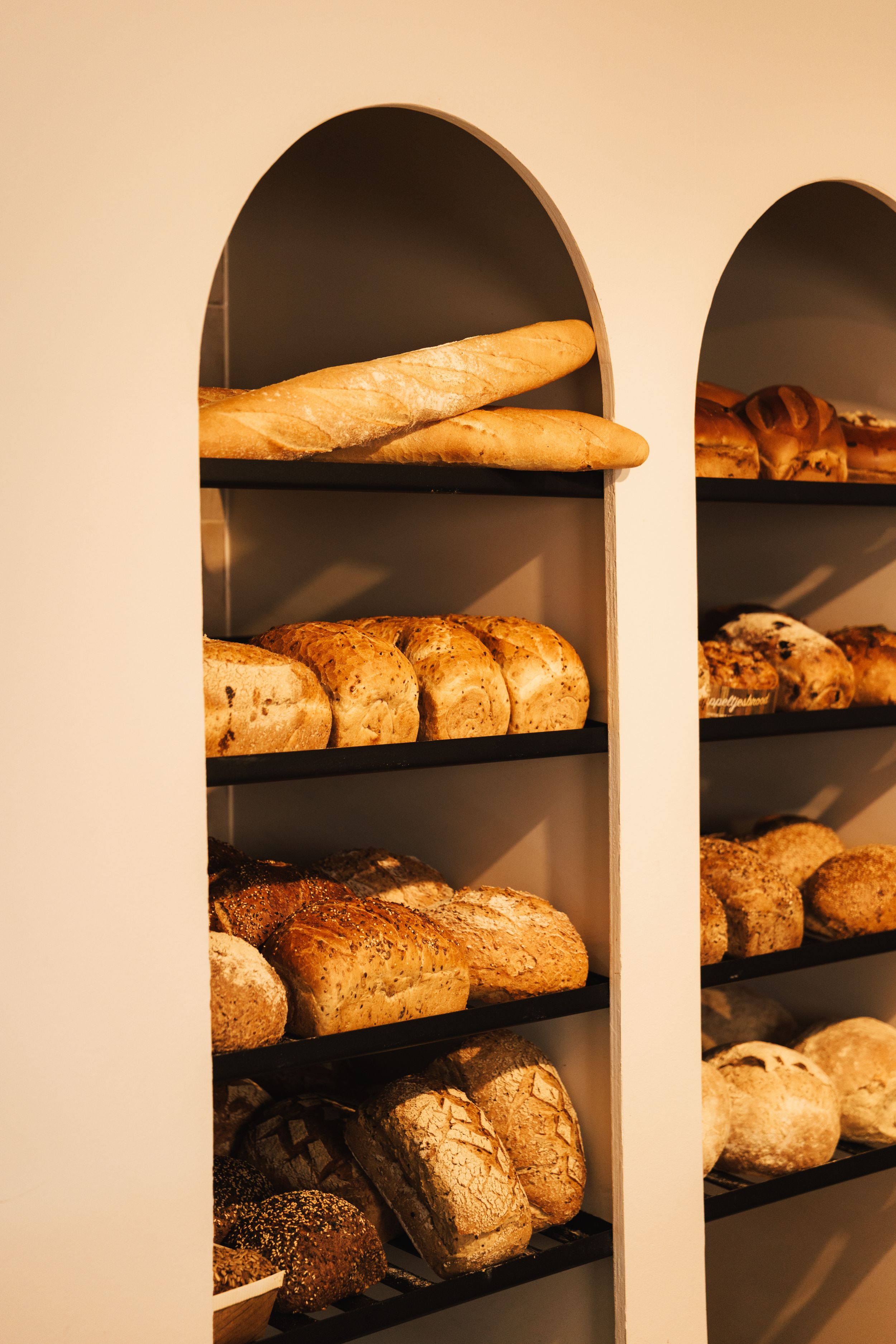 Artisan bakery shelves displaying freshly baked sourdough loaves, baguettes, and crusty bread in arched wall niches.