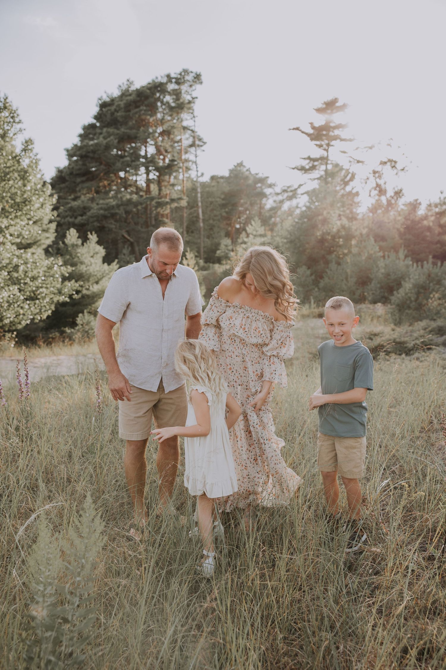 Family of four walking through a sunlit meadow, parents and two children enjoying a golden hour outdoor photoshoot.