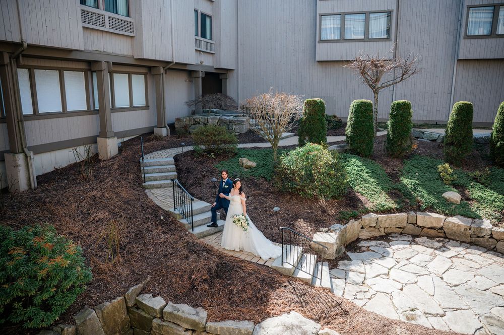 Bride and groom pose in a lush courtyard garden outside a multi-story building on their wedding day at the Heritage Hotel in CT