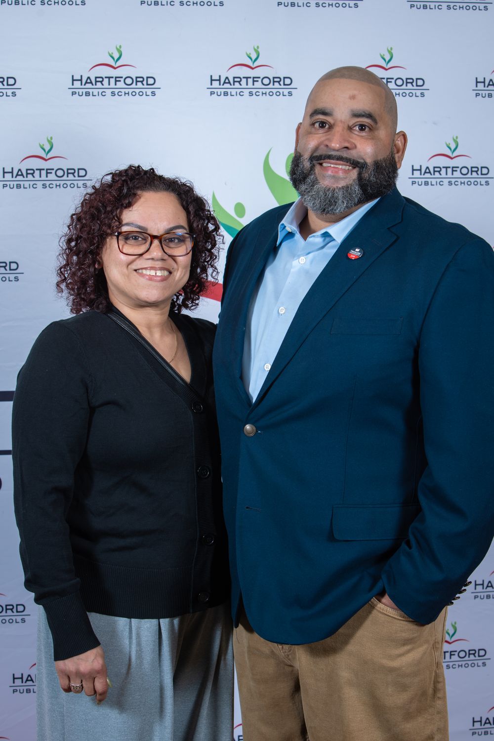 Two professionals smiling together in front of a Hartford Public Schools branded backdrop at an official event.