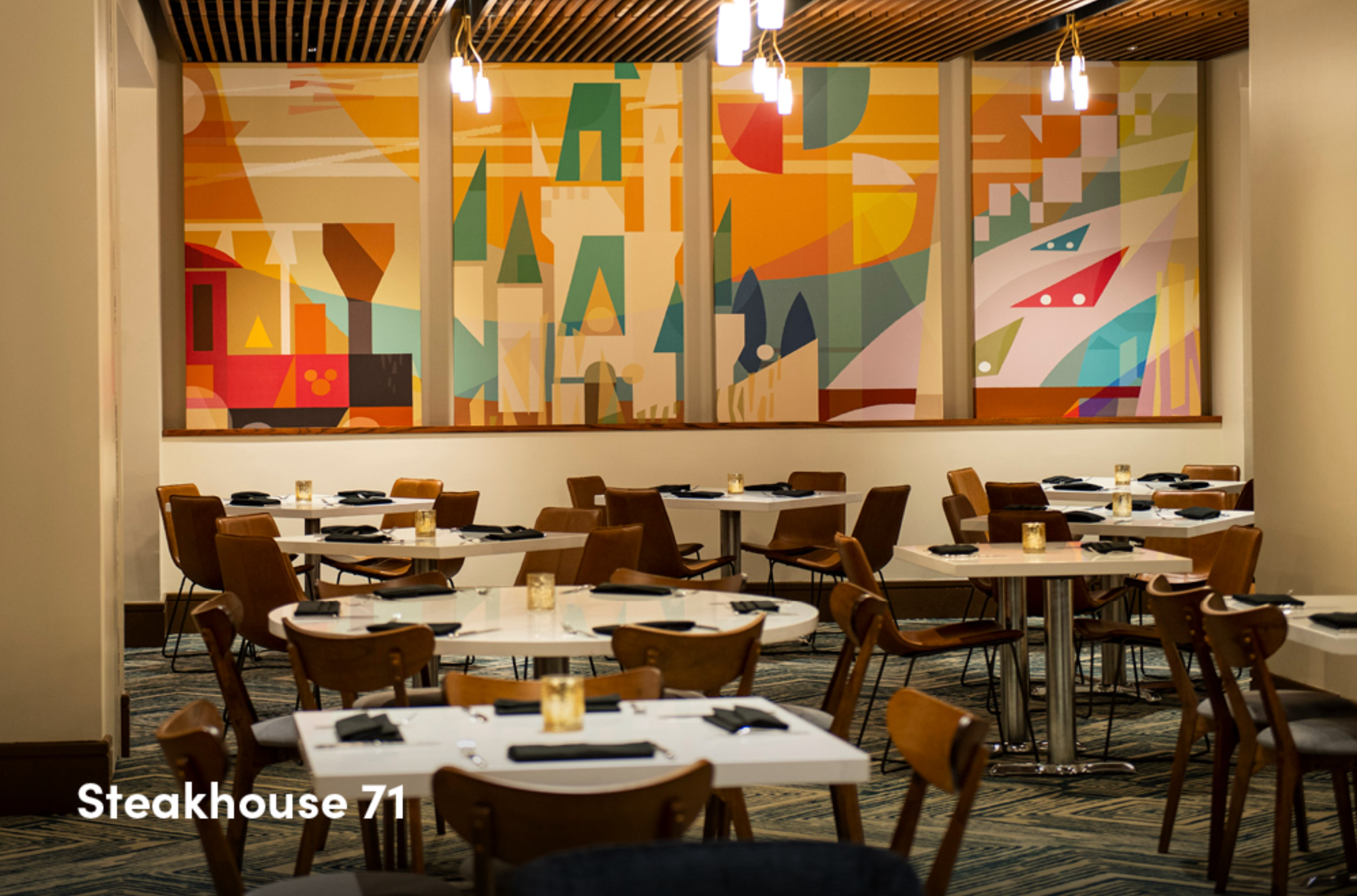 Modern restaurant interior with wooden tables and colorful wall art in warm lighting.