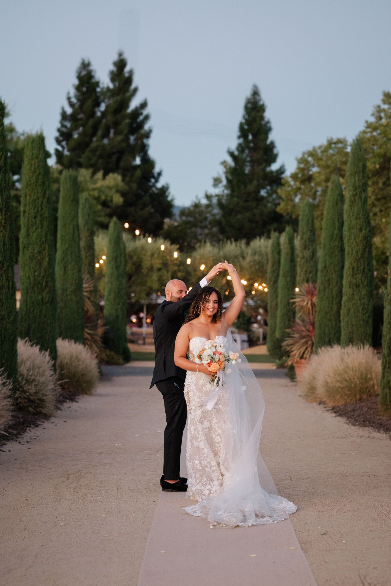 Bride and groom exchange vows at floral arch in vineyard wedding ceremony with mountain backdrop.