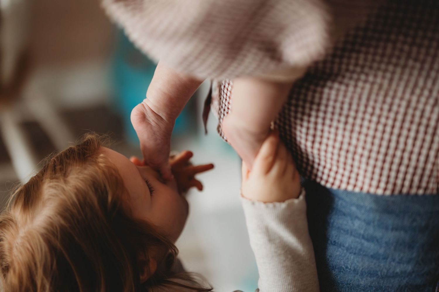 A toddler reaches up toward an adult while being held, captured in a tender and intimate family moment indoors.