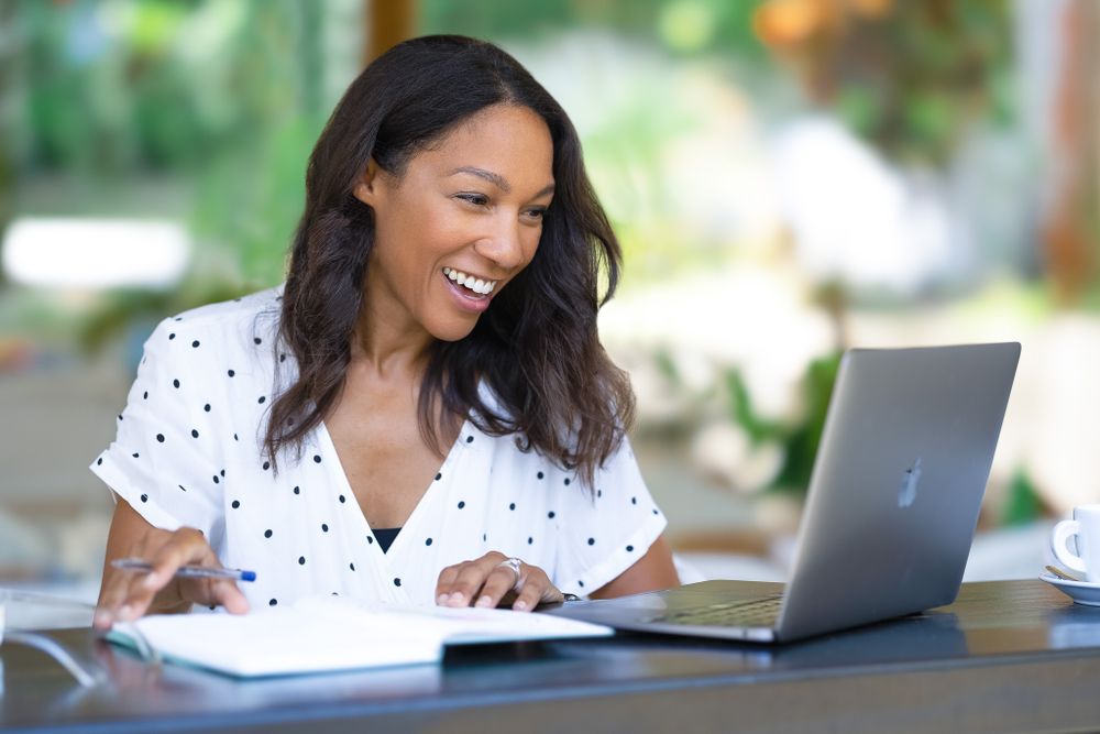 A professional working on a laptop outdoors with a polka dot shirt and bright expression.