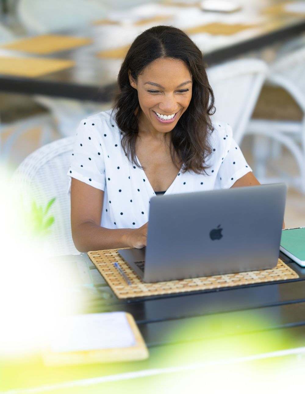 Someone smiling while working on a MacBook laptop wearing a white polka dot top.