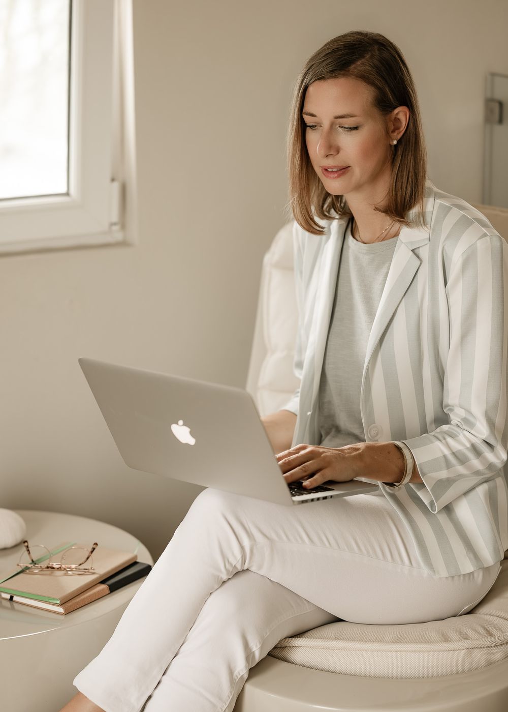 Professional working on laptop in minimalist white office space with natural lighting.