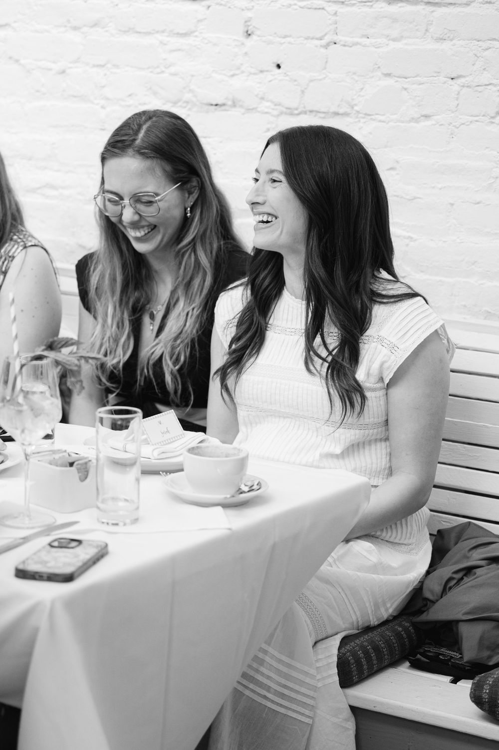 Two women laughing joyfully at a restaurant table in black and white photo.