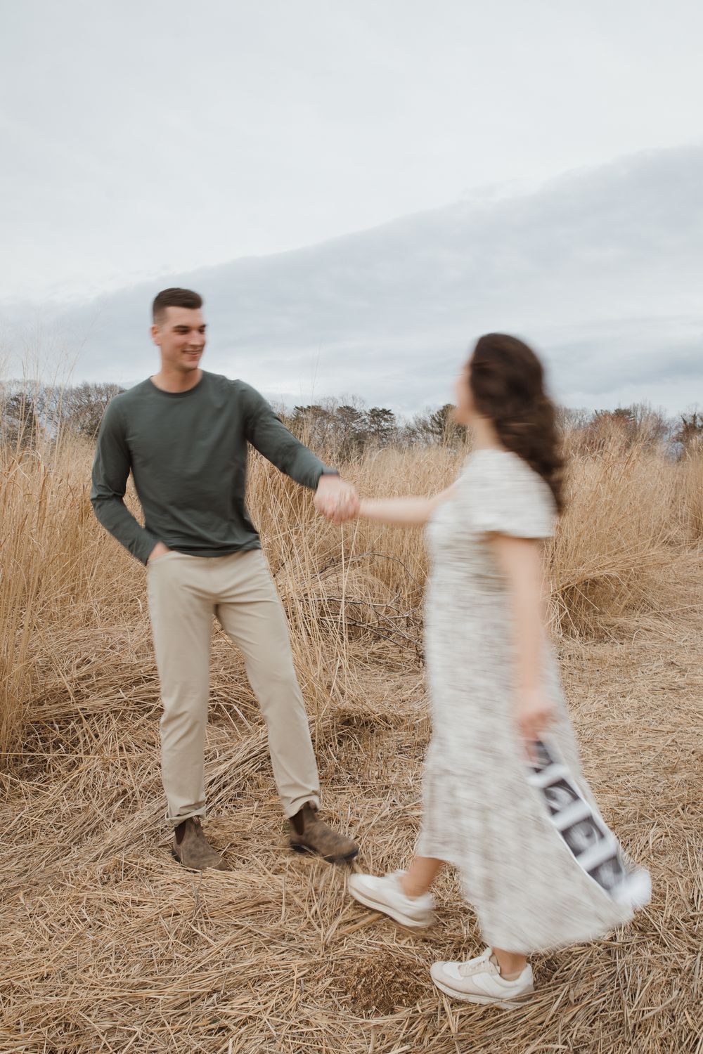 A smiling man in a green shirt holds hands with a woman in a floral dress in a golden field.