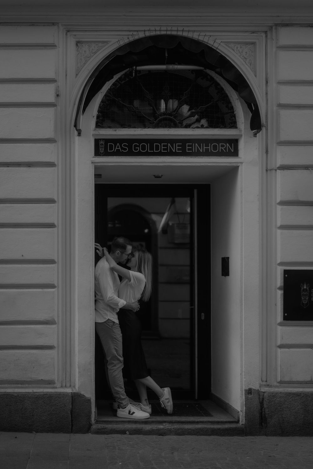Couple sharing a romantic kiss in the doorway of Das Goldene Einhorn in a black and white photo.