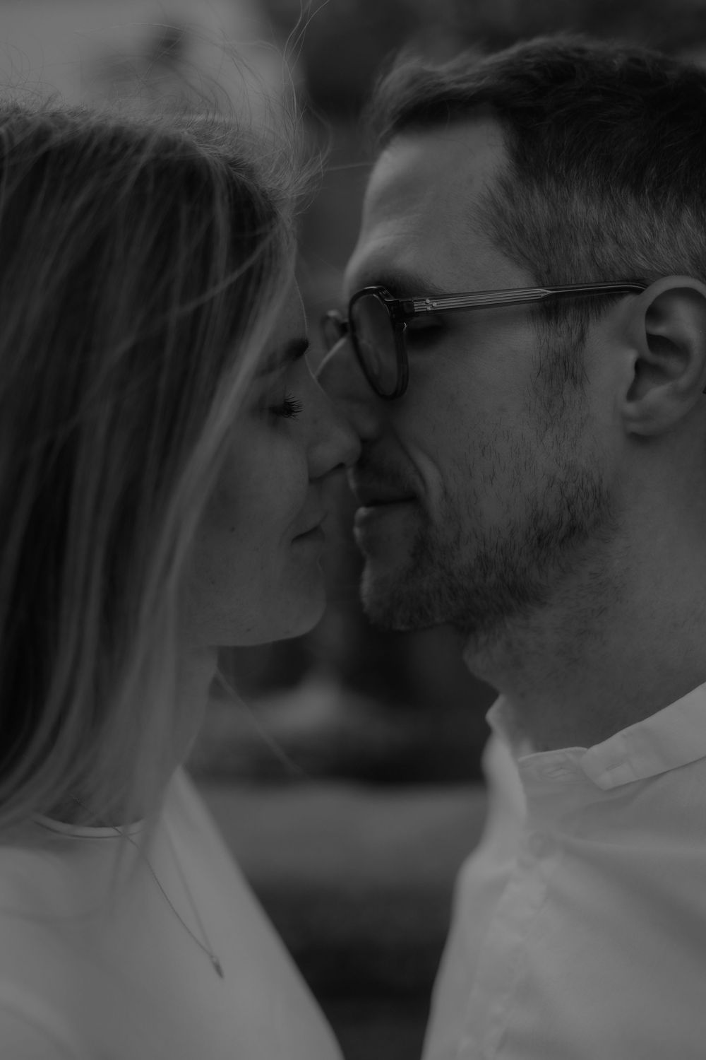 Black and white close-up of a romantic couple about to kiss, man wearing glasses.