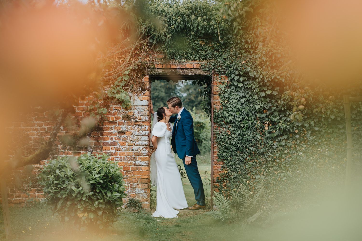 Bride and groom share a romantic moment in an ivy-covered brick doorway surrounded by lush greenery at Standlake Vineyard Reading