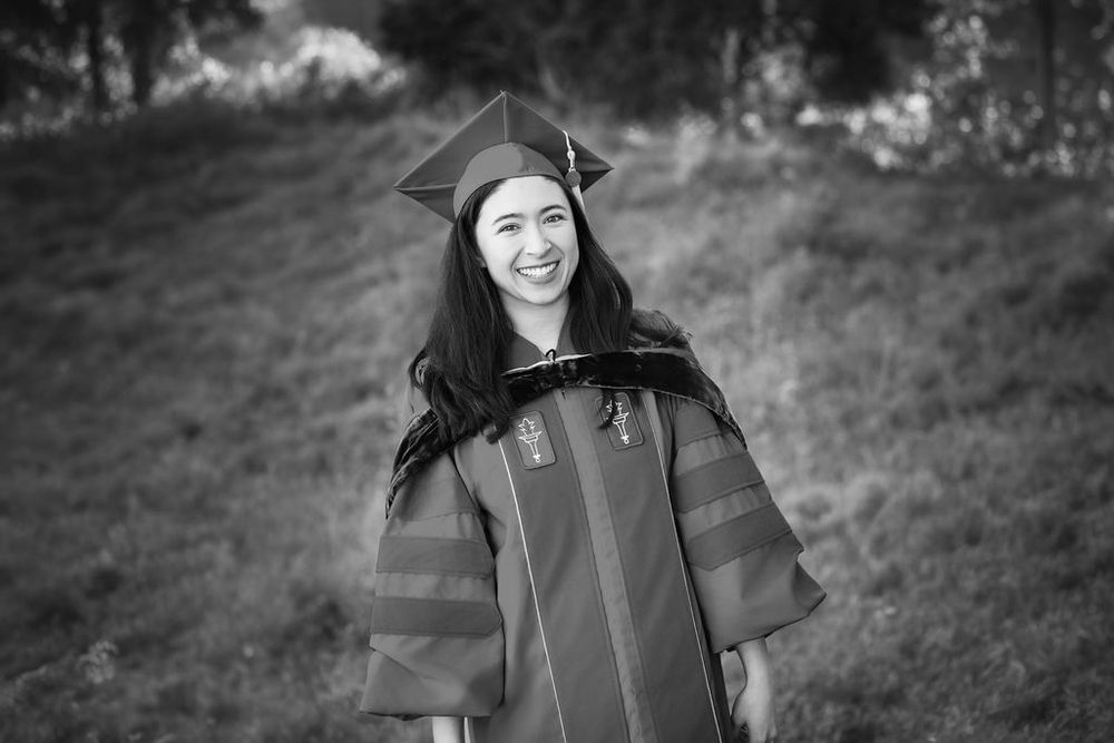 A smiling woman in graduation cap and gown poses outdoors in a black and white photo.