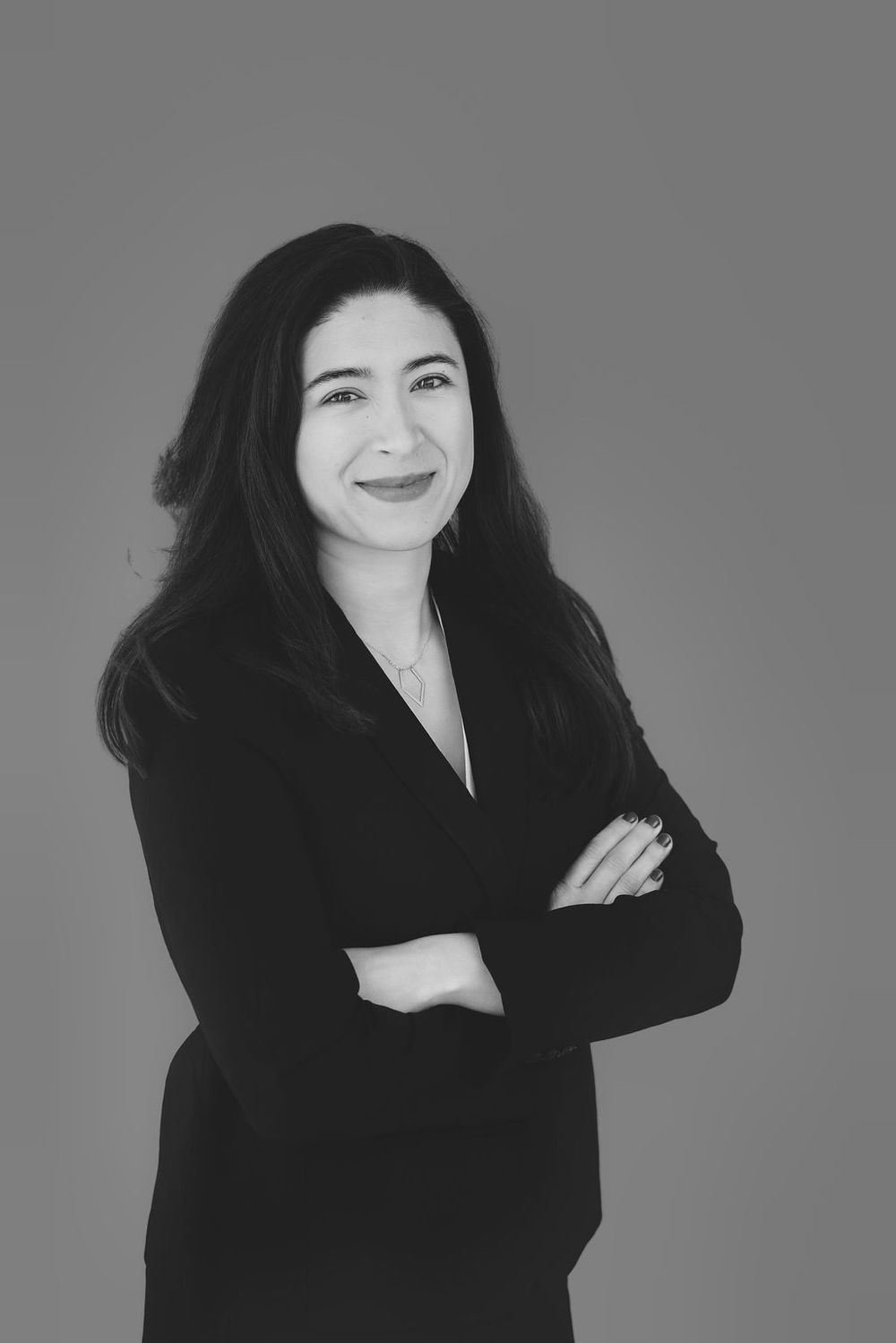 Black and white professional headshot of a smiling woman in a blazer with arms crossed against a gray background.