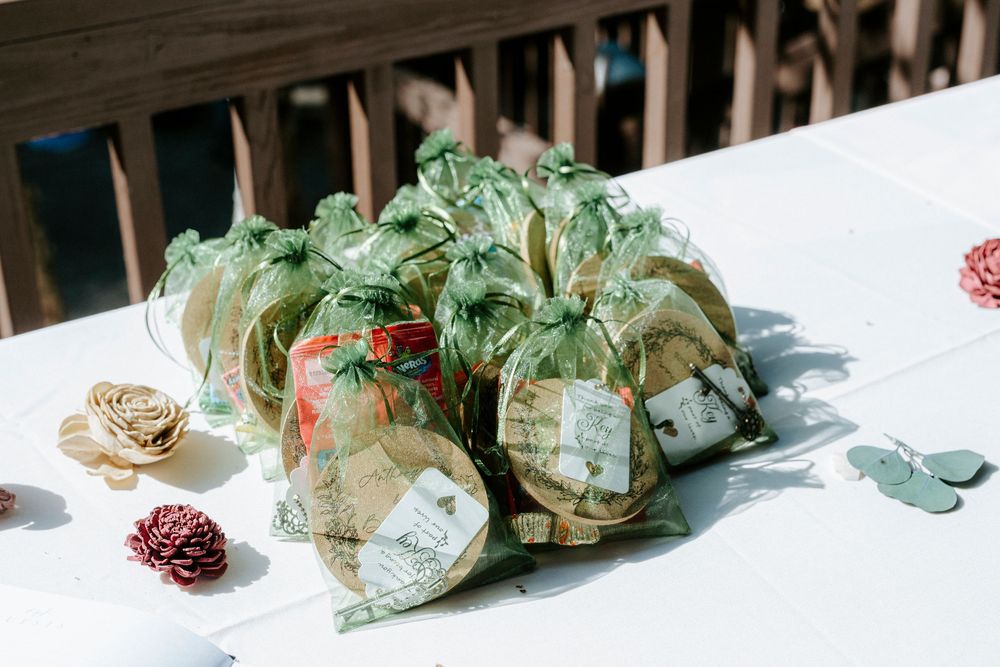 Green organza gift bags with map print tags arranged on a white table as wedding favors outdoors.