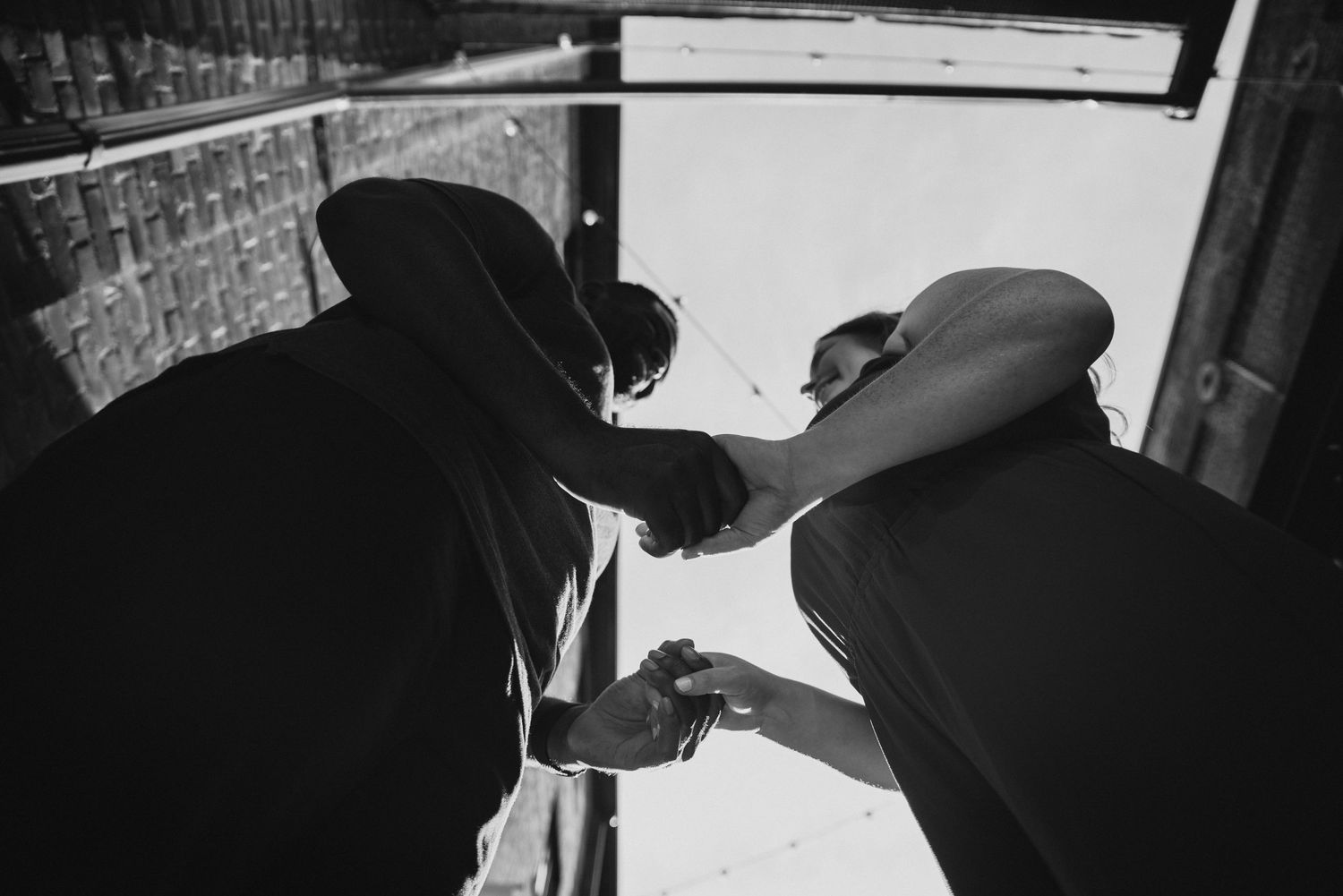 Black and white photo of two people shaking hands viewed from below against a bright sky.