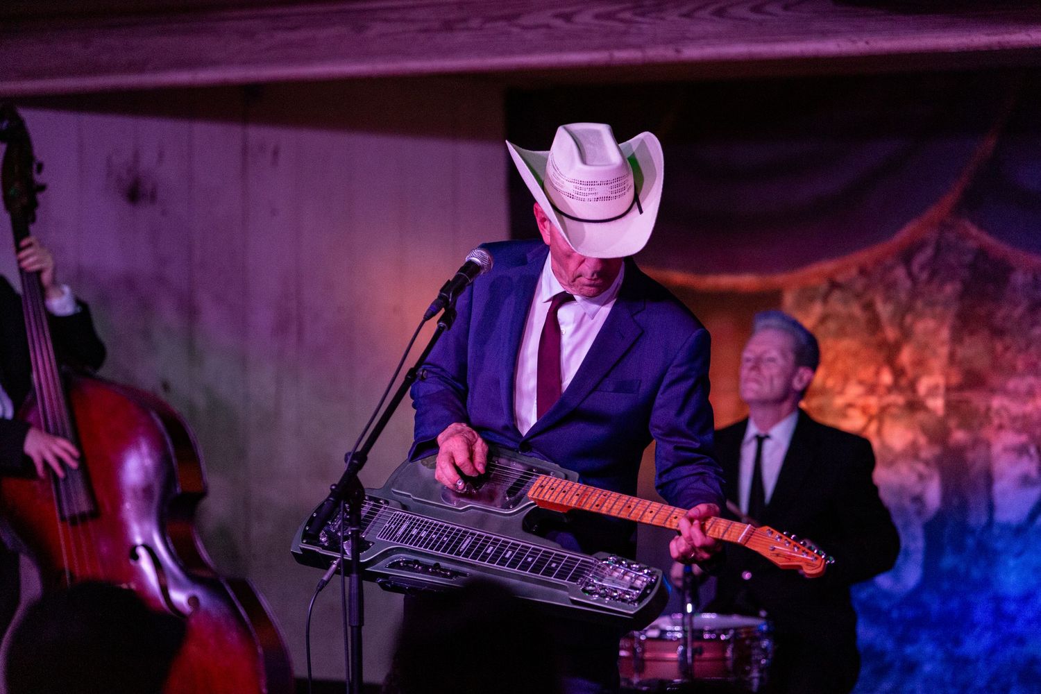 Musician in white cowboy hat plays steel guitar on stage with bassist performing live country music.