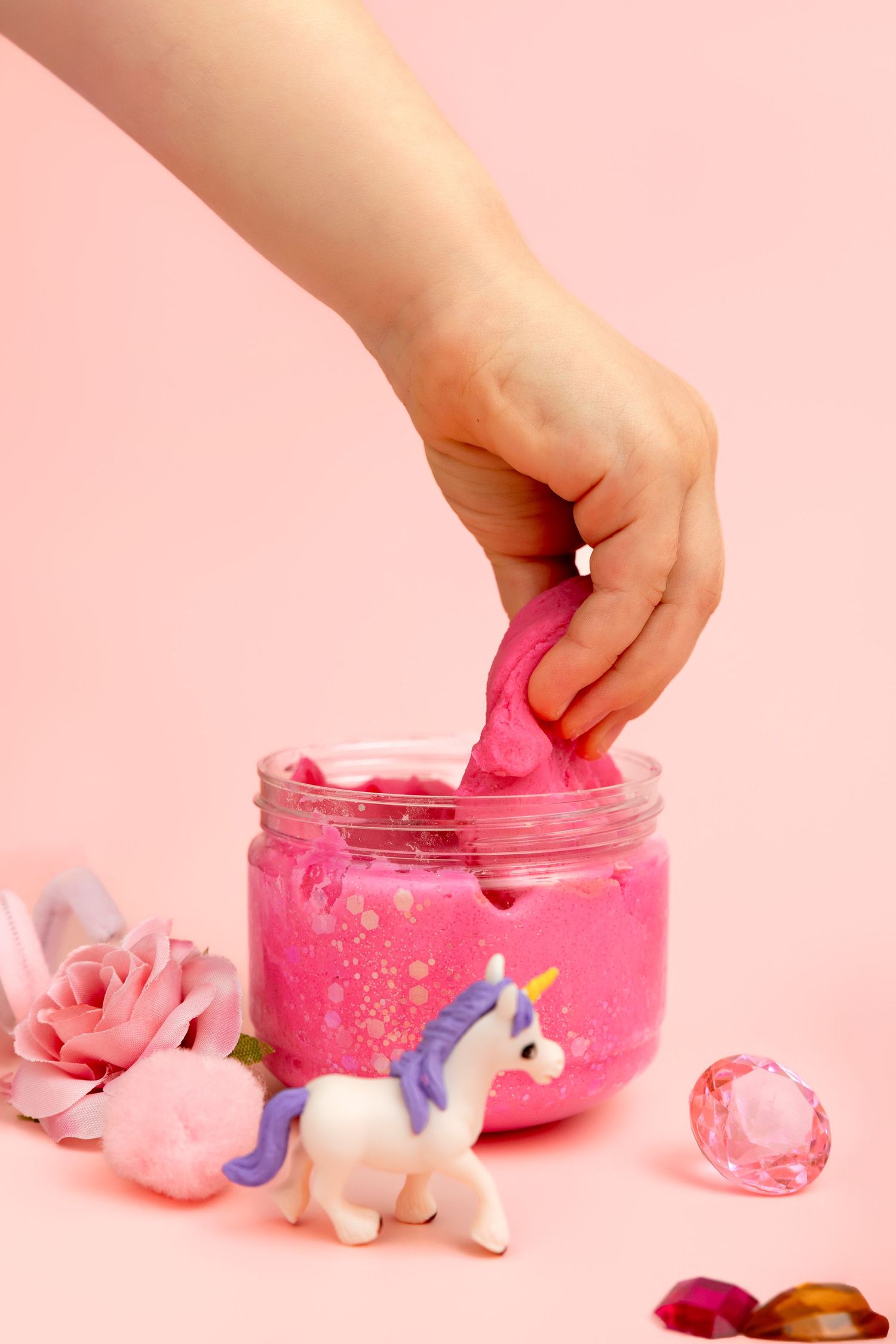 Young girl in floral dress playing with pastel silicone tea set cups and teapot on white background.