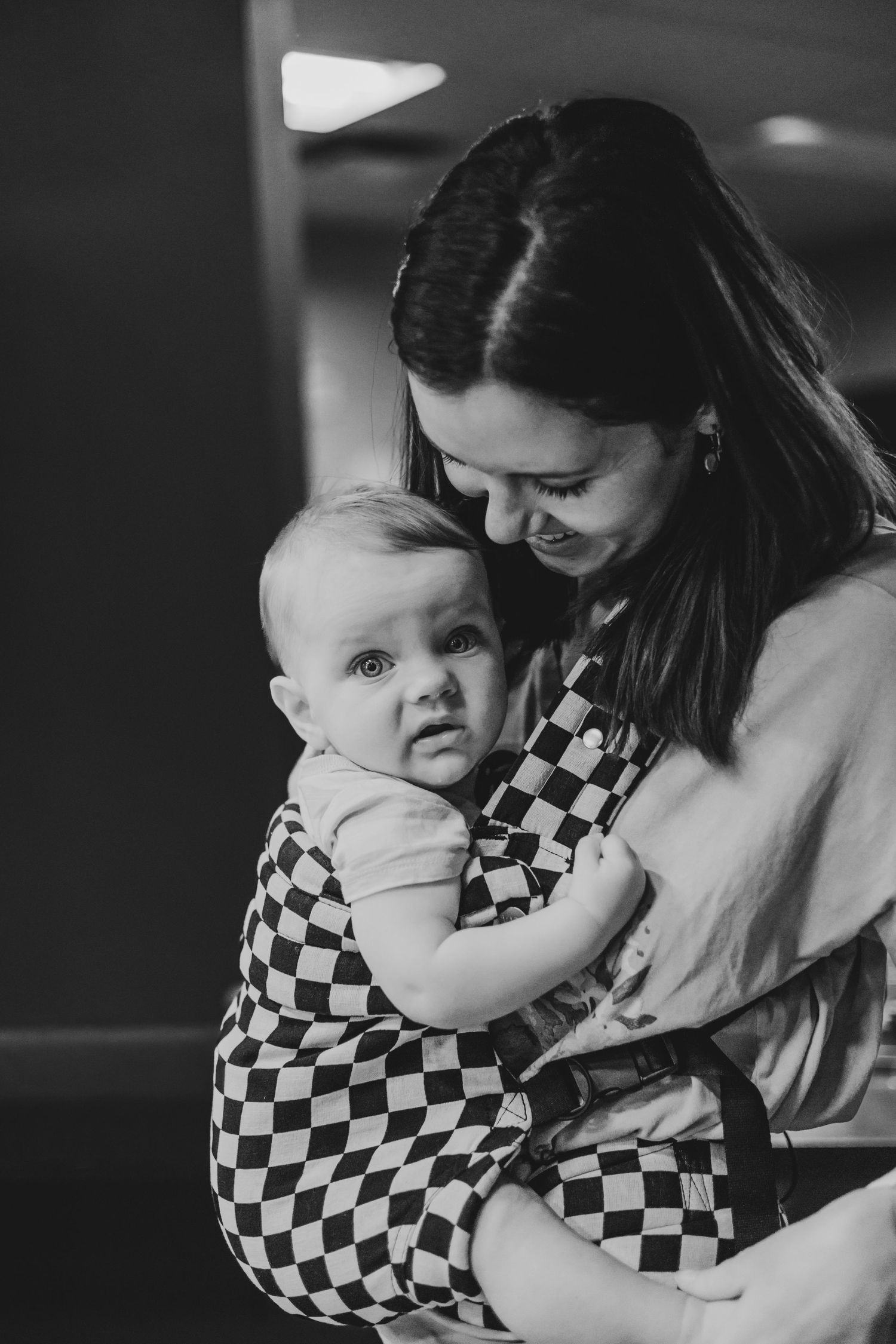 Black and white photo of a smiling mother tenderly holding her baby in a checkered outfit.