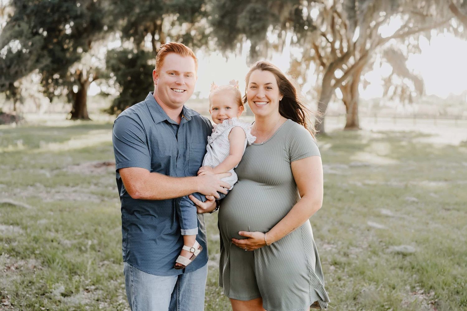 A family of three posing together outdoors in a park setting during golden hour.