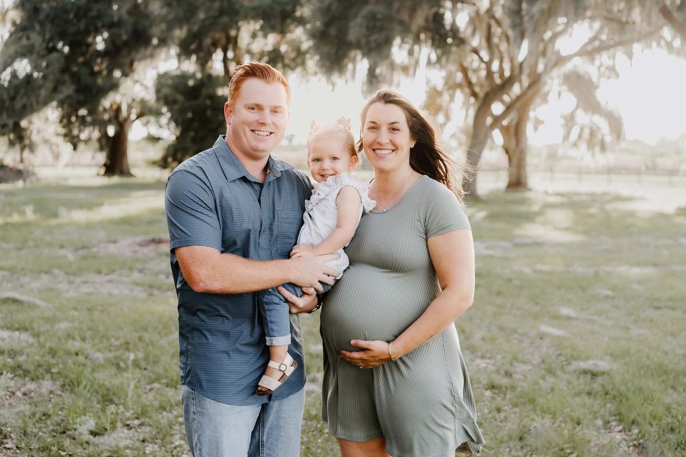 A family of three posing together outdoors in a park setting during golden hour.