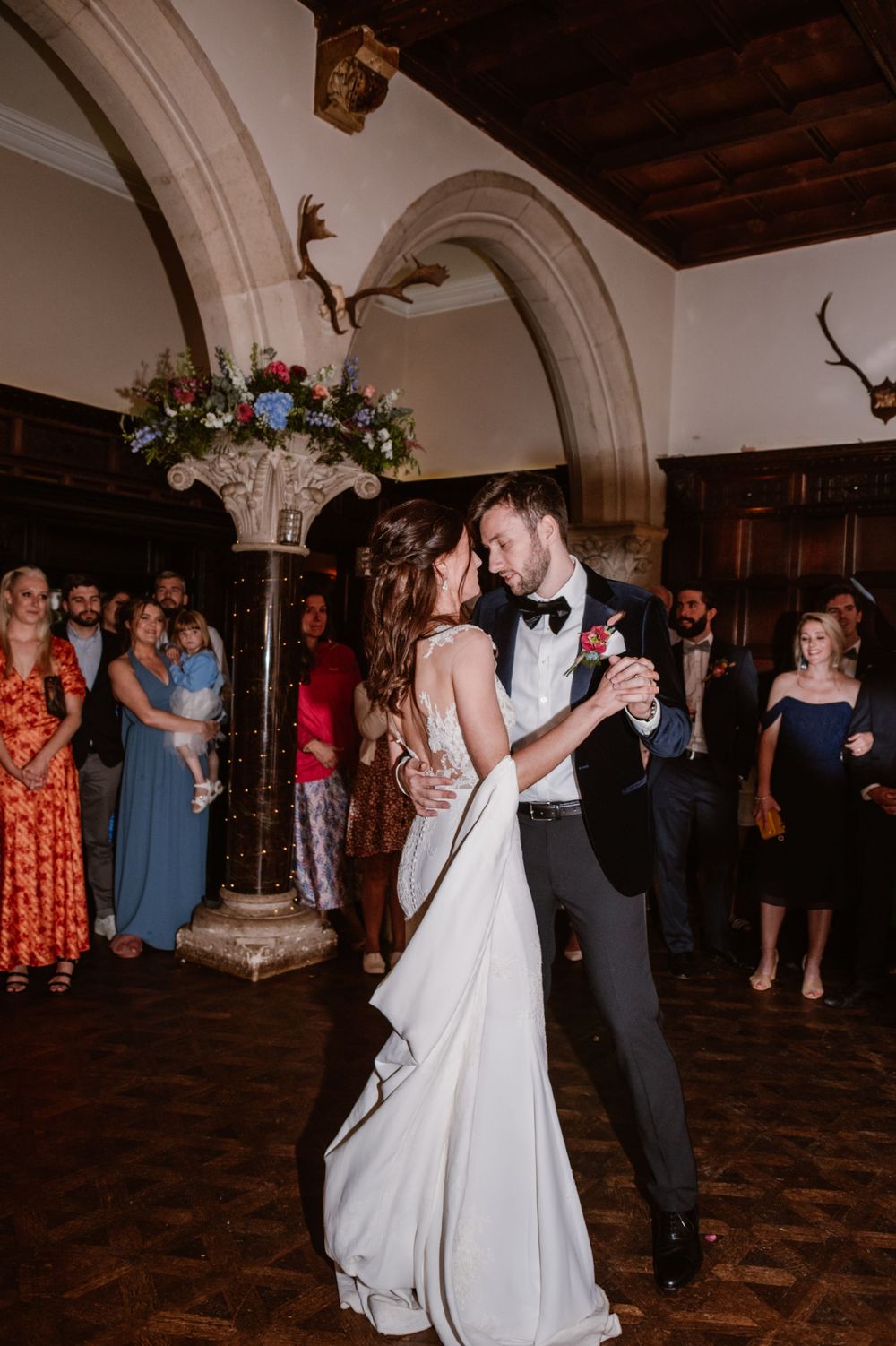 Bride and groom share their first dance in an elegant castle ballroom surrounded by wedding guests.