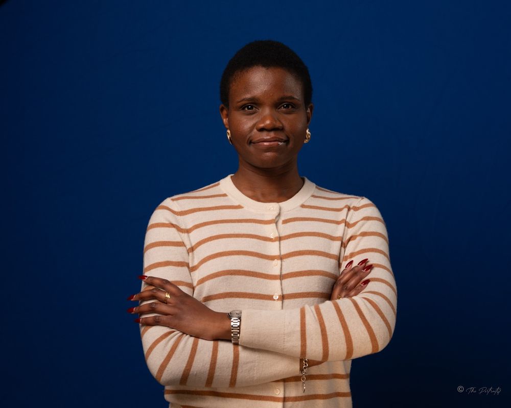 Woman in striped sweater with arms crossed against blue background.