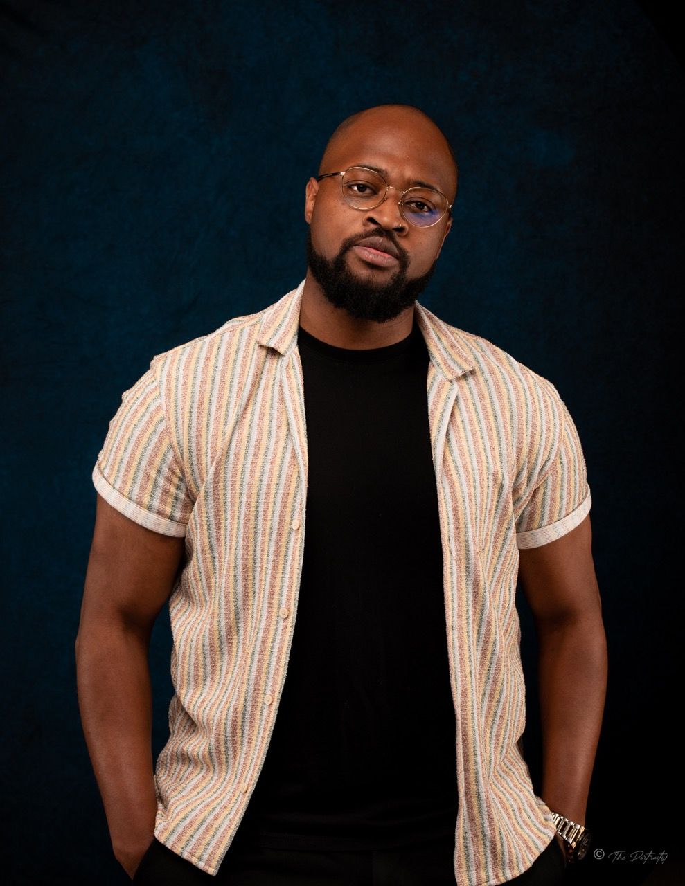 Bald man with beard in striped shirt against dark blue background.