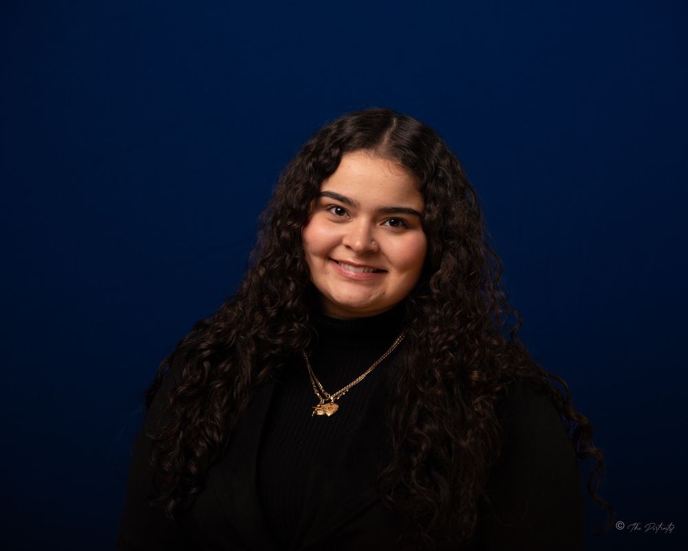 Young woman with curly hair smiling against blue background.