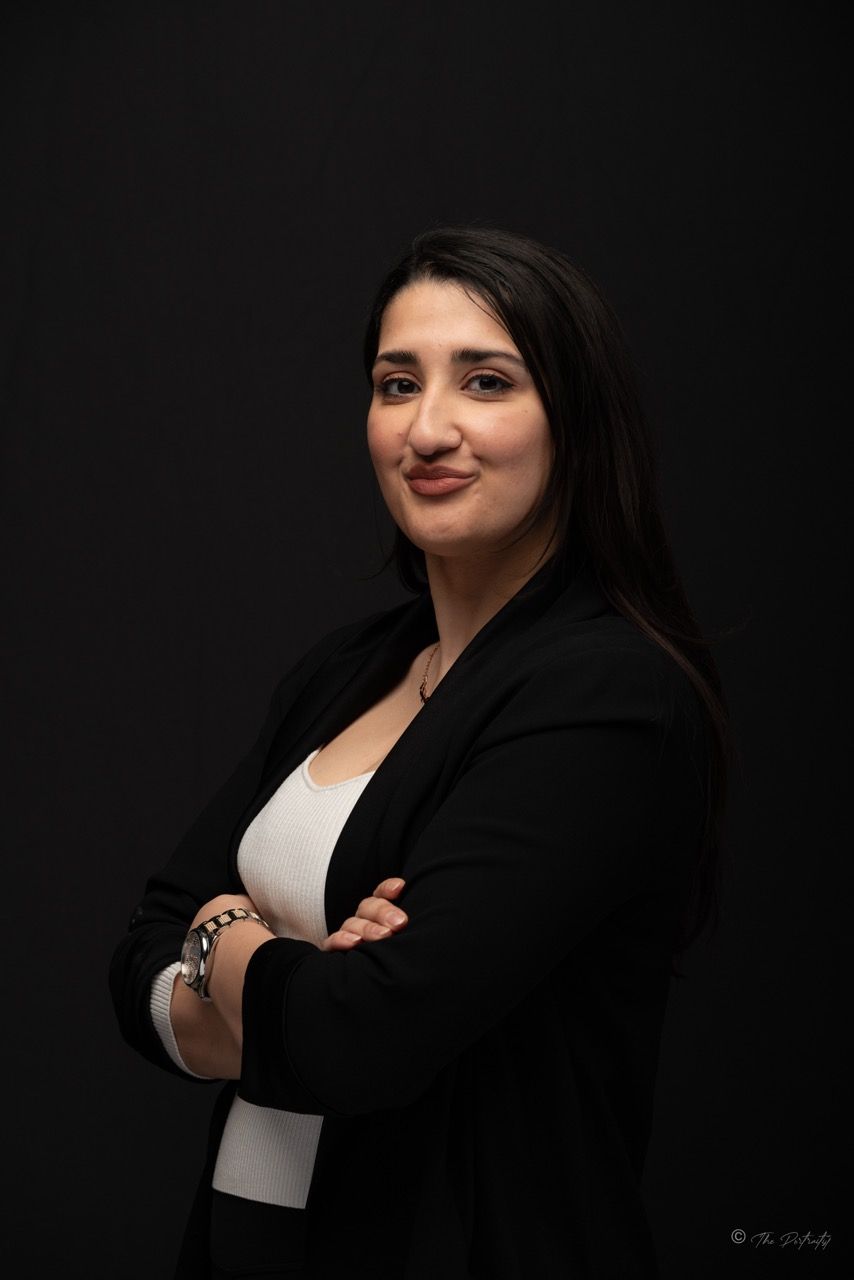 Woman in black blazer with arms crossed against black background.