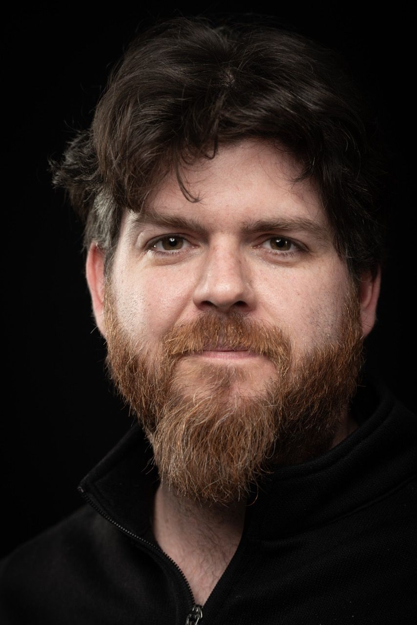 Man with red beard in black hoodie against black background.