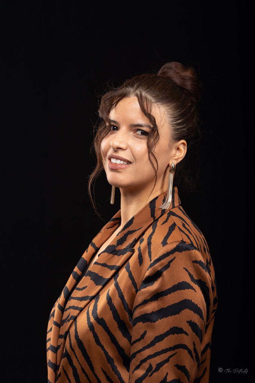 Smiling woman in tiger print top with hair up and long earrings poses against black background.