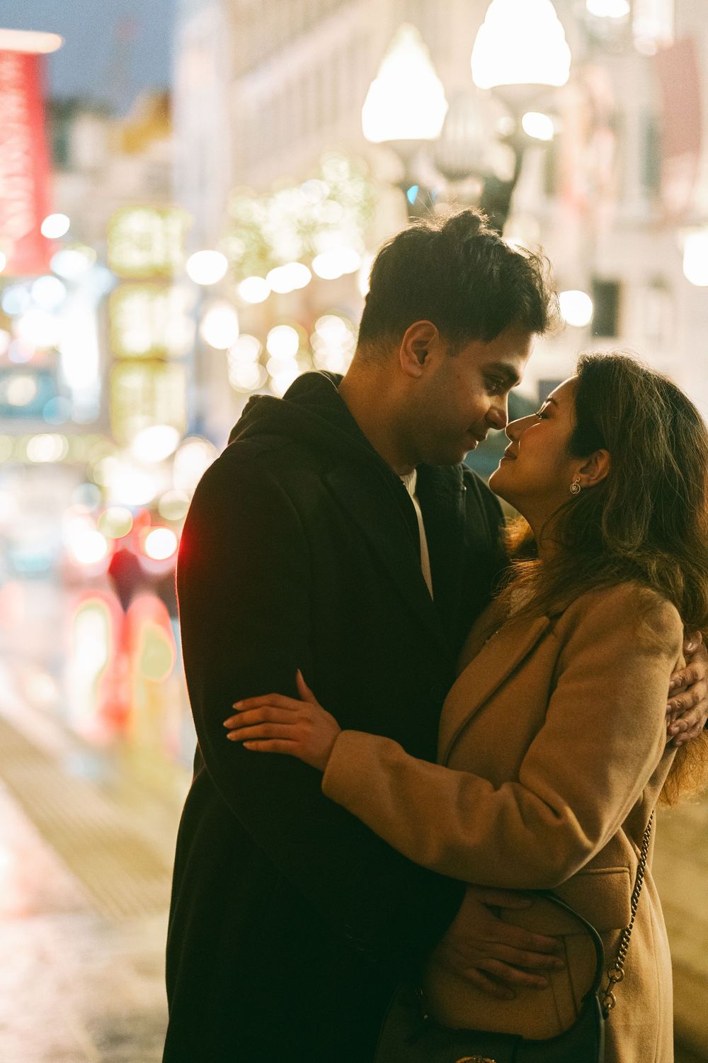 Romantic couple embracing and about to kiss on a city street at night with bokeh lights in the background.