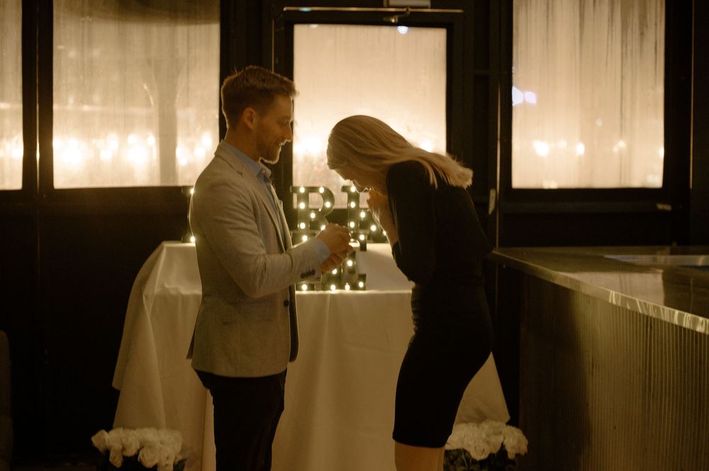 Couple sharing a romantic candlelit dinner moment, man in gray blazer and woman in black dress holding hands.