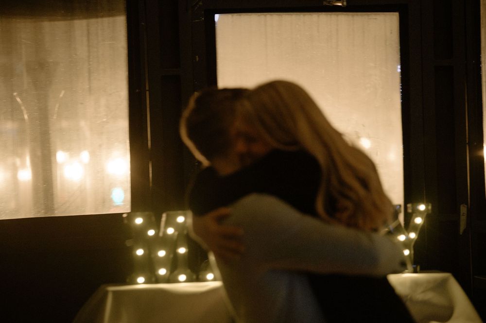 Couple sharing an emotional embrace after a marriage proposal in a warmly lit romantic setting.