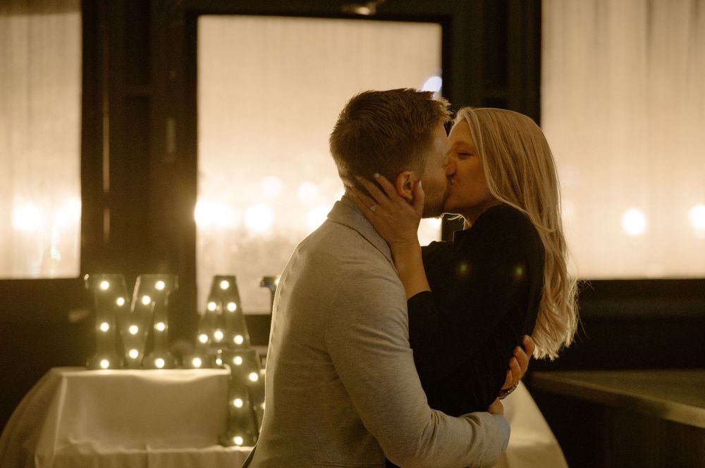 Couple sharing a passionate kiss surrounded by glowing candles and decorative lights in a romantic setting.