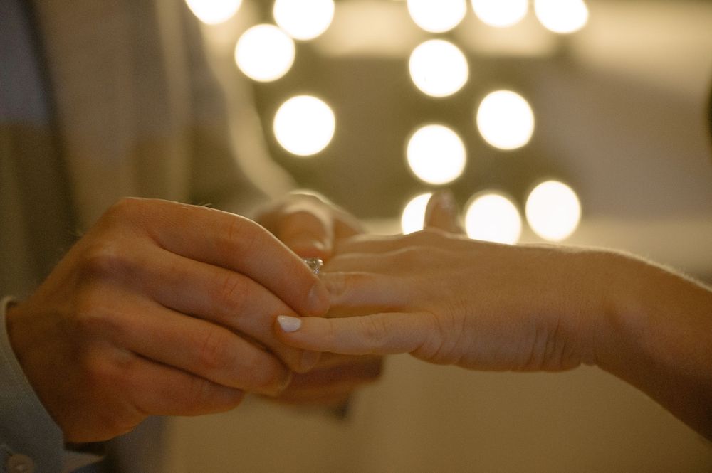 Close-up of a romantic marriage proposal with a ring being placed on a finger, with soft bokeh lights in the background.