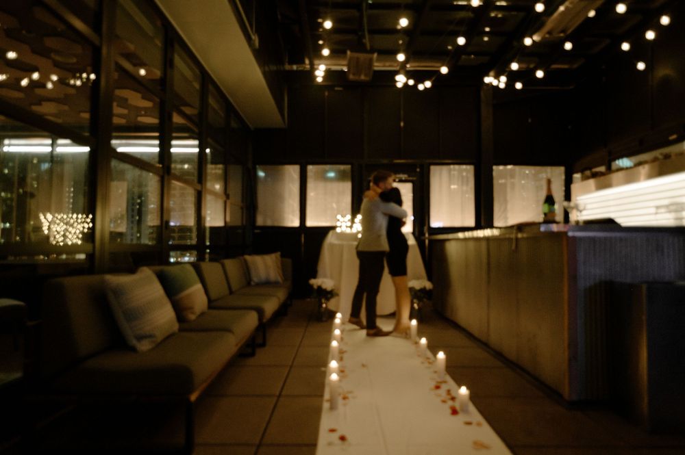 Couple sharing a romantic moment in a candlelit restaurant with string lights and rose petals on the floor.