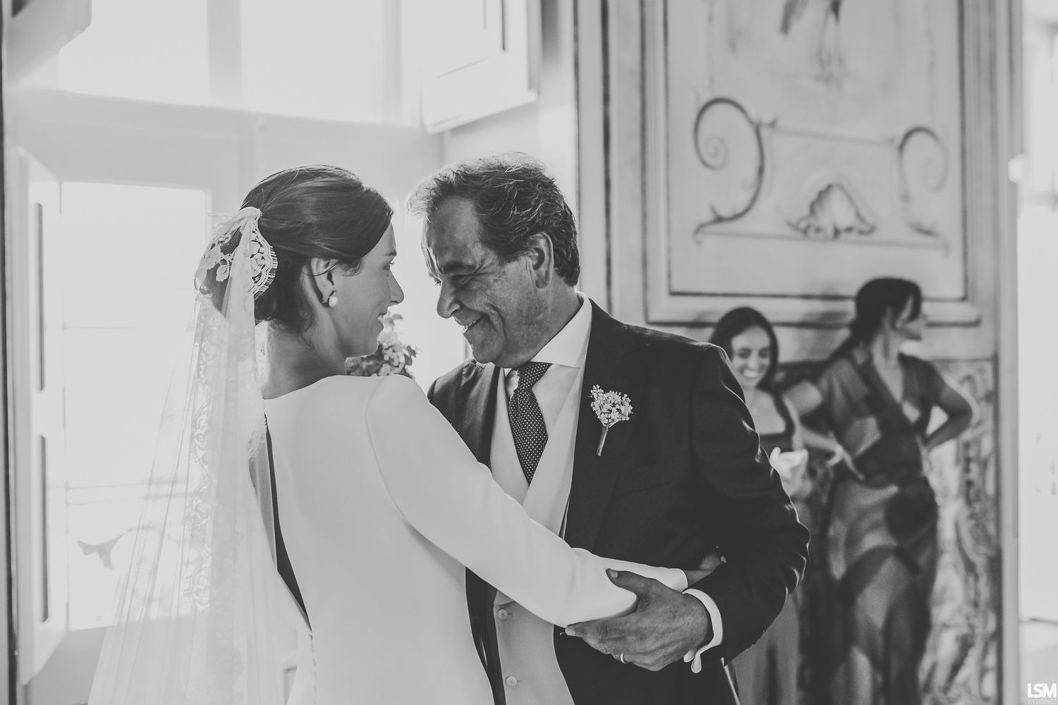 Black and white wedding photo of bride and older man sharing a tender dance moment at elegant venue.