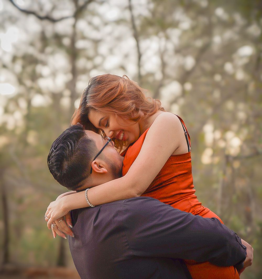 Couple sharing a romantic moment in forest, man lifting woman in orange dress as she smiles joyfully.